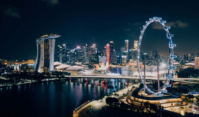 Panorama of Singapore skyline by night, with lighted Singapore Flyer, one of the biggest Ferris wheels in the world, in the foreground; photo by Chuttersnap, Unsplash.