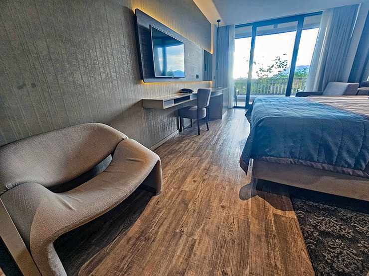 Armchair, TV, work desk, and bed in the room of Hotel Jama Postojna, Slovenia, with large glass sliding doors opening the view toward nature; photo by Ivan Kralj.