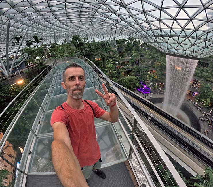 Travel blogger Ivan Kralj standing on the Mastercard Canopy Bridge in Jewel, Changi Airport, with the world's largest indoor waterfall in the background; photo by Ivan Kralj.