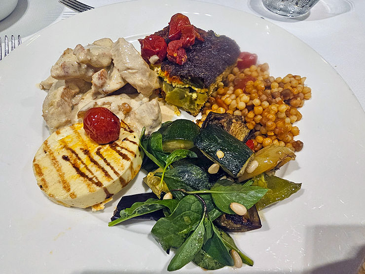 A plate with grilled cheese with roasted tomatoes, zucchini with baby spinach and pine nuts, vegetable casserole, fregola sarda with Mediterranean veggies, and turkey strips in the cream-peanut sauce, at buffet dinner in Hotel Jama's Magical Garden Restaurant in Postojna, Slovenia; photo by Ivan Kralj.