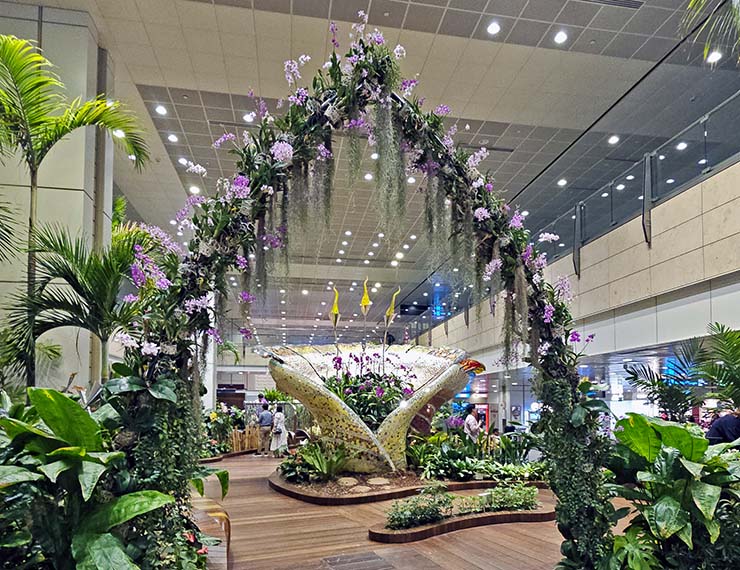 Timber decking path through the Enchanted Garden with a floral arch, and a glass bouquet sculpture filled with seasonal flowers, one of the attractions of Signapore Changi Airport's Terminal 2; photo by Ivan Kralj.