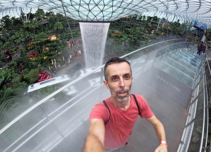 Pipeaway travel blogger Ivan Kralj taking a selfie at Mastercard Canopy Bridge at Jewel Changi Airport in Singapore, with the Rain Vortex and Shiseido Forest Valley in the background.