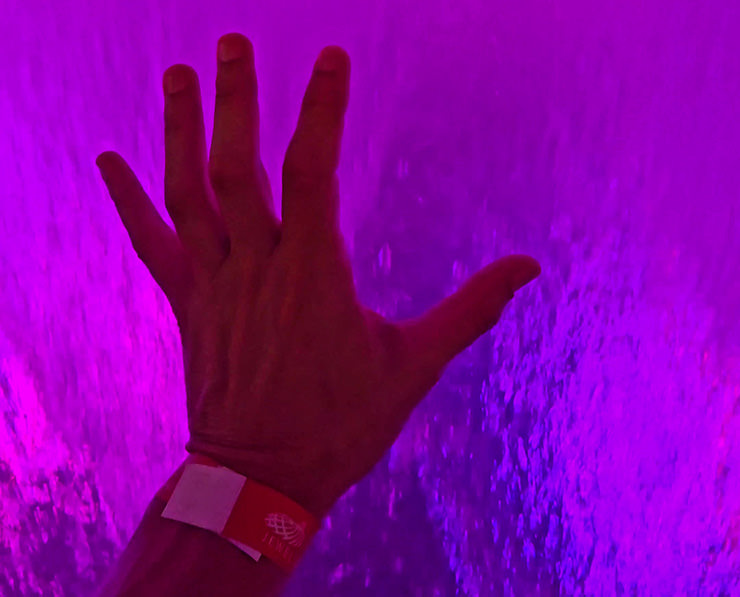 Hand touching the magenta-colored acrylic tank of the Rain Vortex waterfall in Jewel Changi Airport, Singapore; photo by Ivan Kralj.