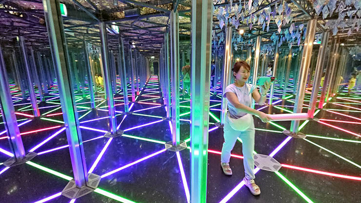 Woman walking with a pink foam stick through the kaleidoscopic Mirror Maze in Canopy Park, Jewel Changi Airport in Singapore; photo by Ivan Kralj.